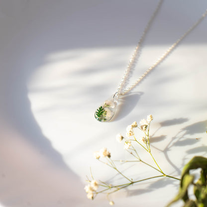 A collection of handmade resin art pendants, showcasing intricate floral designs preserved in clear resin, attached to delicate necklaces.