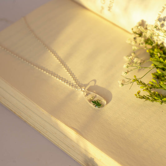 A collection of handmade resin art pendants, showcasing intricate floral designs preserved in clear resin, attached to delicate necklaces.