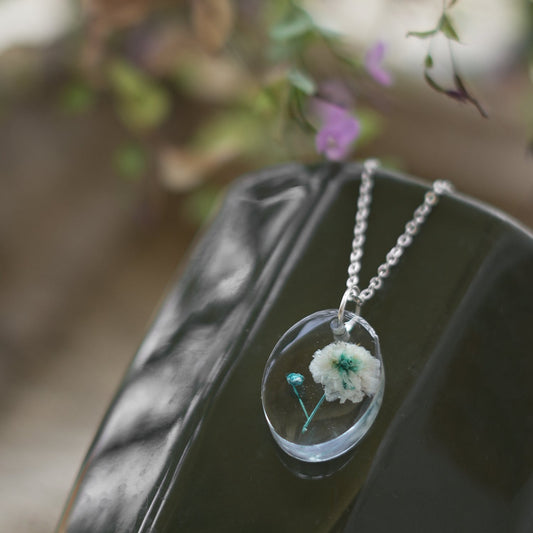 A collection of handmade resin art pendants, showcasing intricate floral designs preserved in clear resin, attached to delicate necklaces.