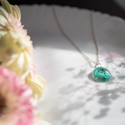 A collection of handmade resin art pendants, showcasing intricate floral designs preserved in clear resin, attached to delicate necklaces.