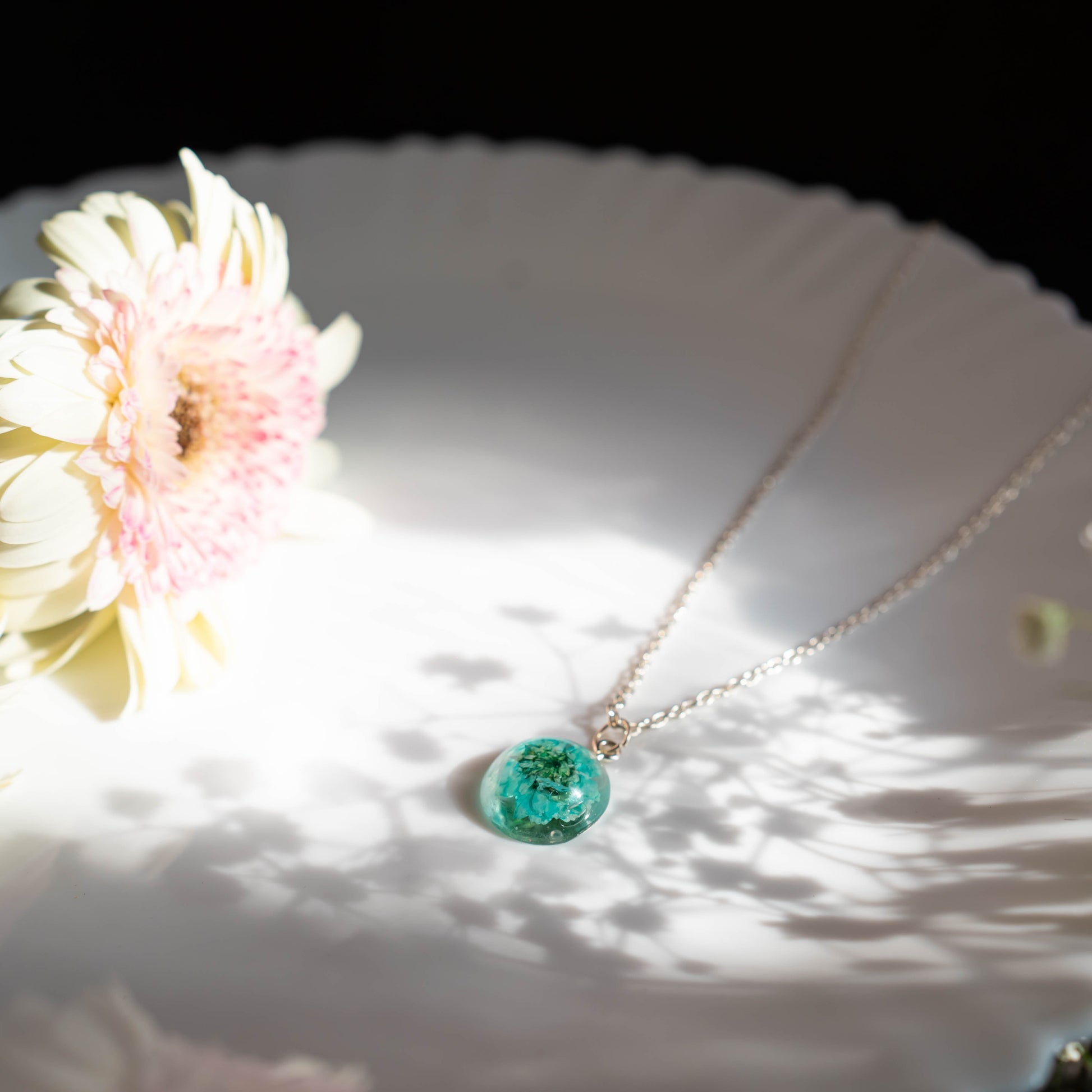 A collection of handmade resin art pendants, showcasing intricate floral designs preserved in clear resin, attached to delicate necklaces.