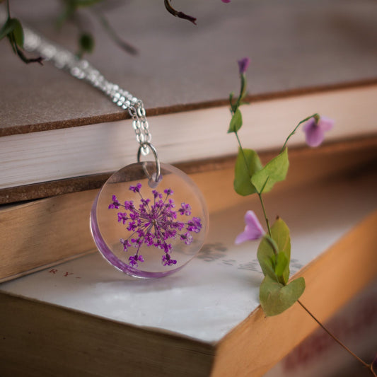 A collection of handmade resin art pendants, showcasing intricate floral designs preserved in clear resin, attached to delicate necklaces.
