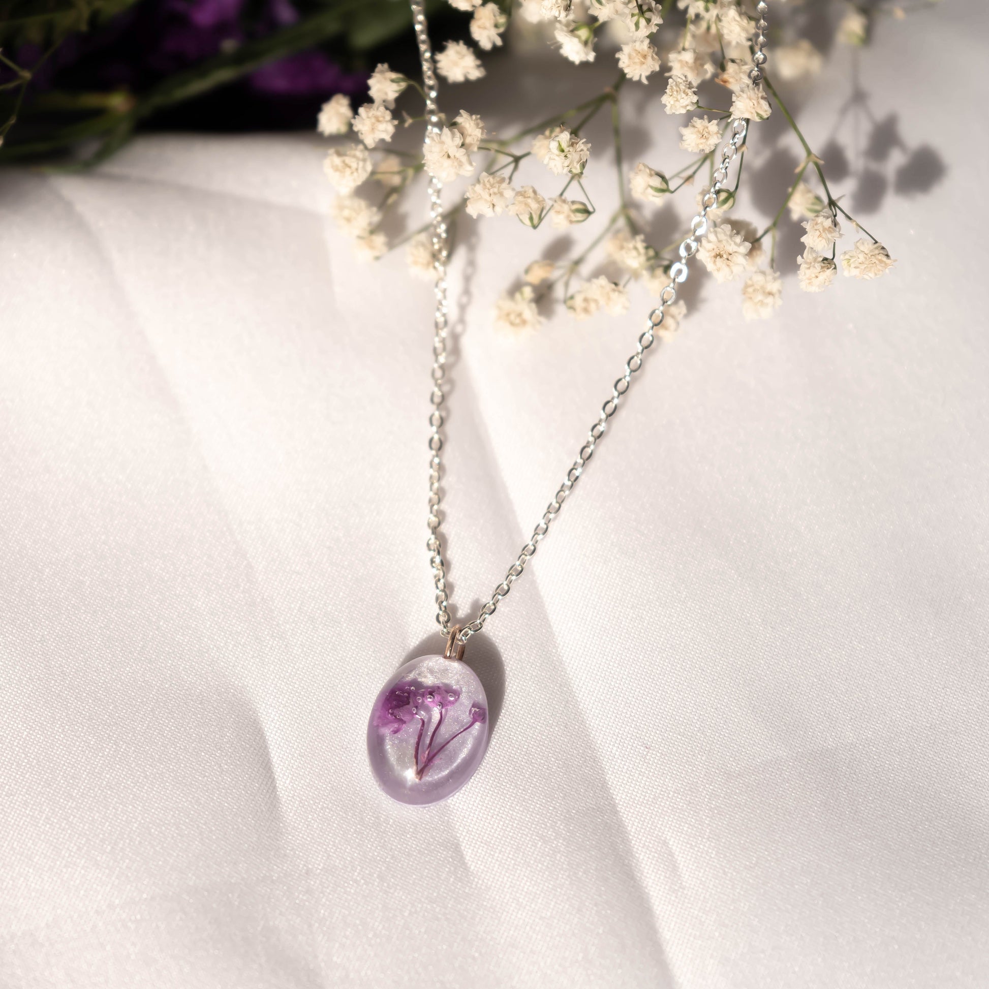 A collection of handmade resin art pendants, showcasing intricate floral designs preserved in clear resin, attached to delicate necklaces.