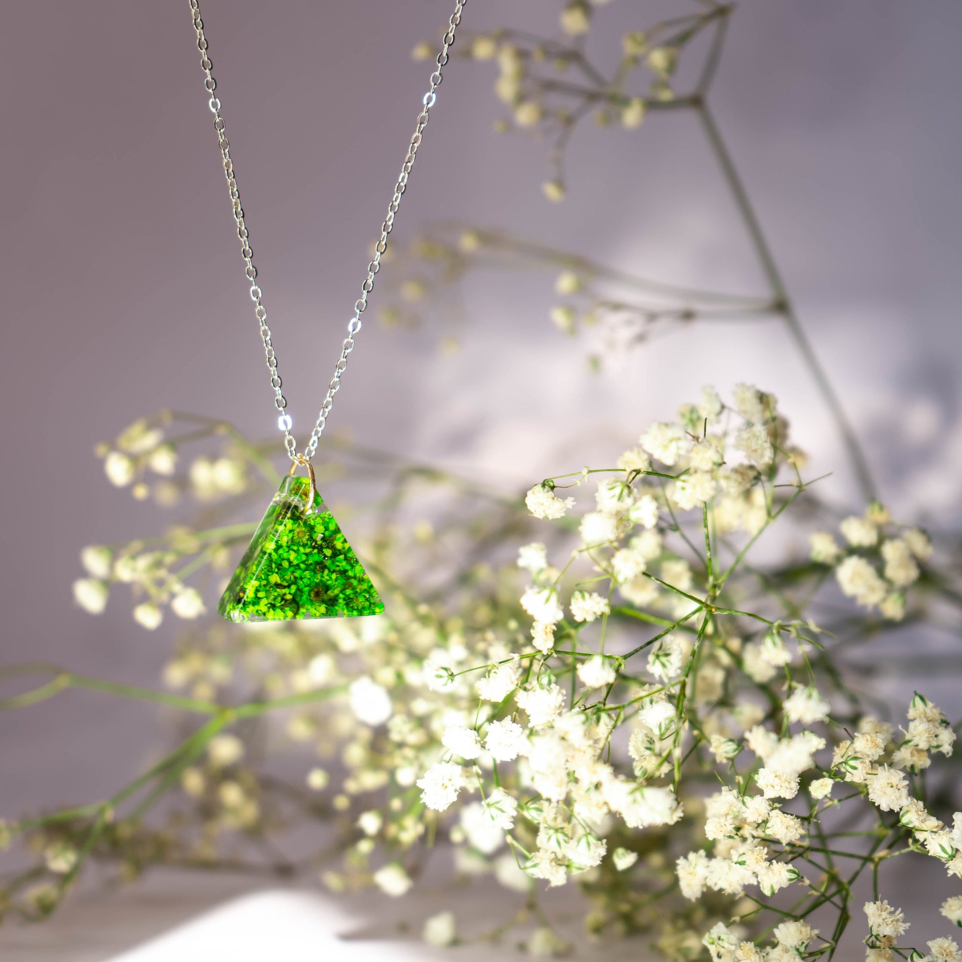 A collection of handmade resin art pendants, showcasing intricate floral designs preserved in clear resin, attached to delicate necklaces.