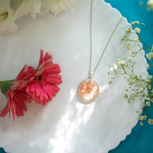 A collection of handmade resin art pendants, showcasing intricate floral designs preserved in clear resin, attached to delicate necklaces.