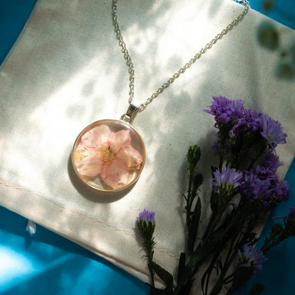 A collection of handmade resin art pendants, showcasing intricate floral designs preserved in clear resin, attached to delicate necklaces.