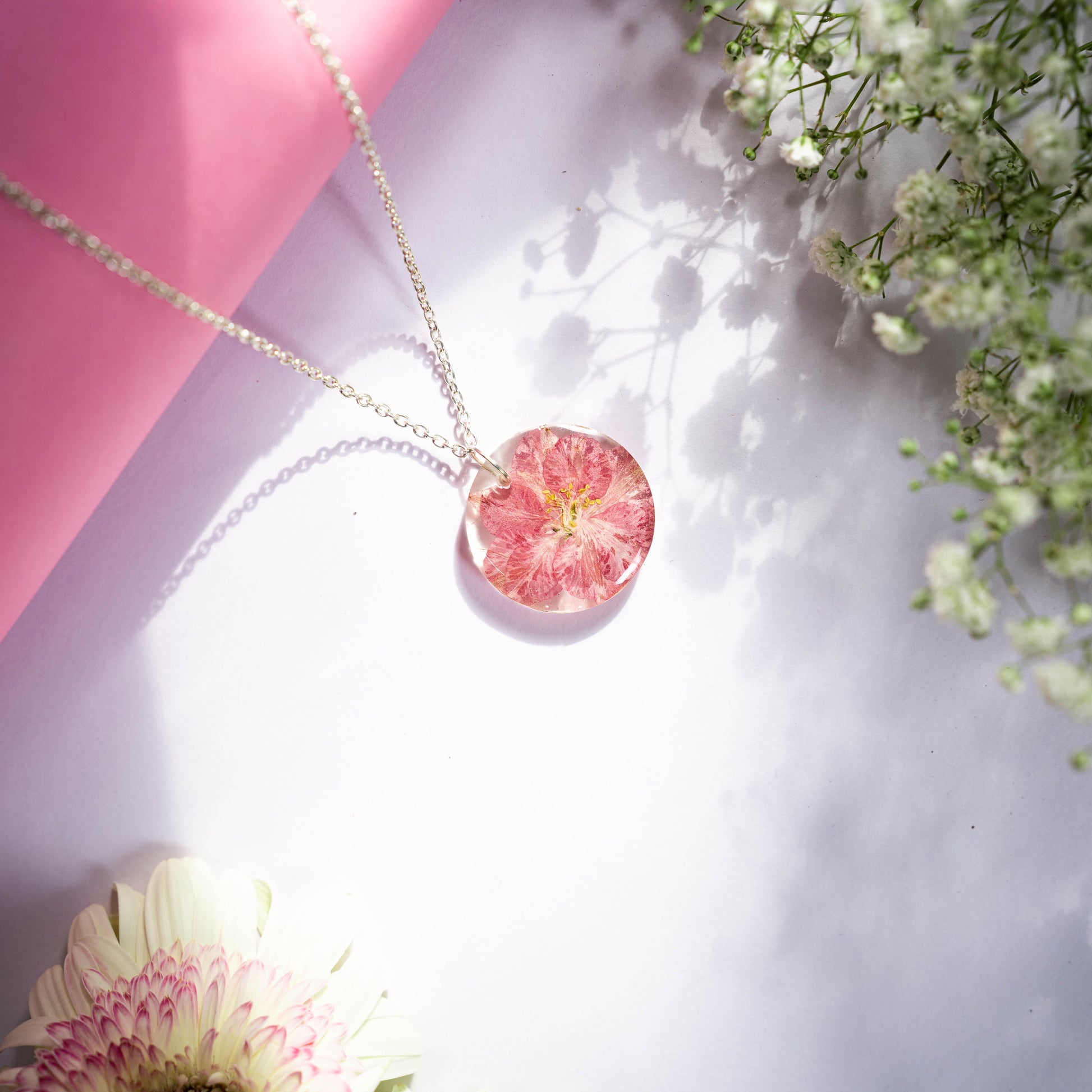 A collection of handmade resin art pendants, showcasing intricate floral designs preserved in clear resin, attached to delicate necklaces.