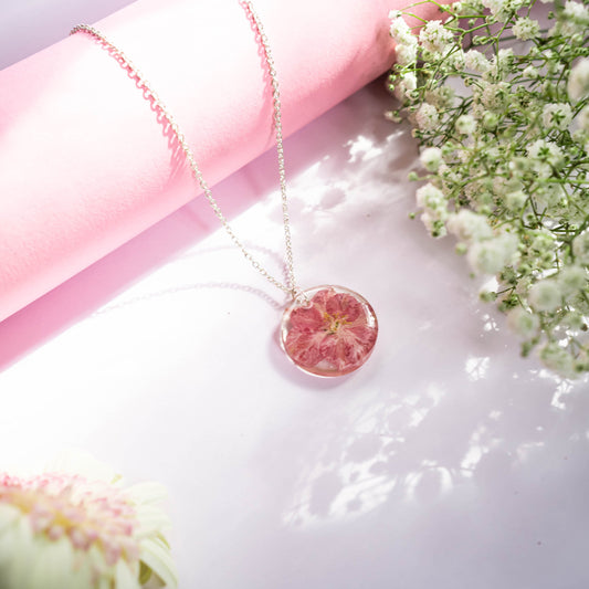 A collection of handmade resin art pendants, showcasing intricate floral designs preserved in clear resin, attached to delicate necklaces.