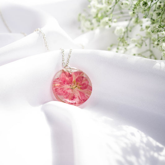 A collection of handmade resin art pendants, showcasing intricate floral designs preserved in clear resin, attached to delicate necklaces.