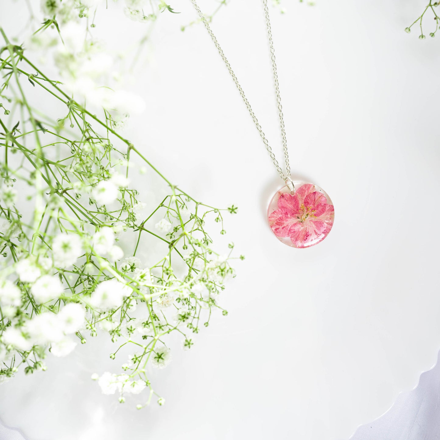 A collection of handmade resin art pendants, showcasing intricate floral designs preserved in clear resin, attached to delicate necklaces.