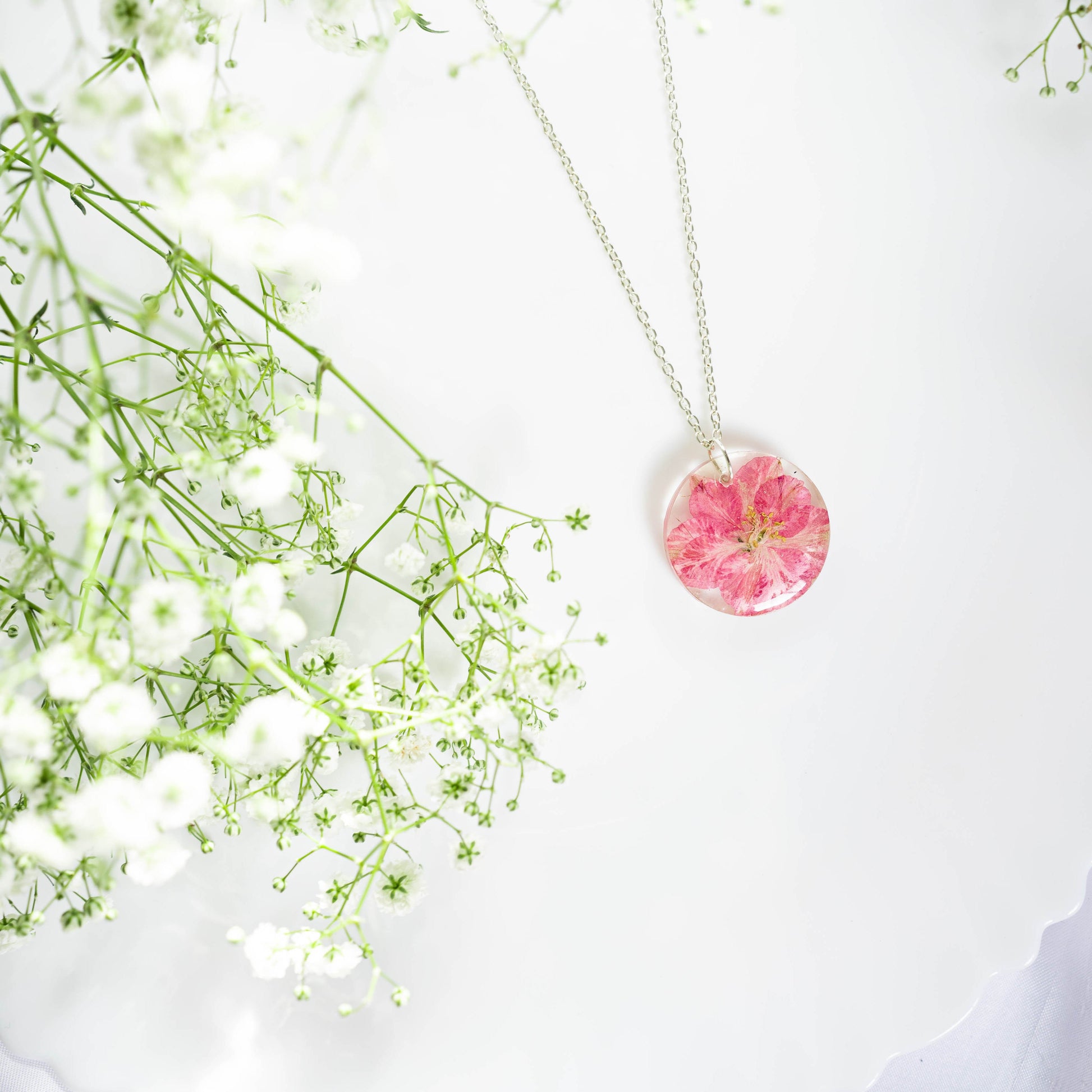 A collection of handmade resin art pendants, showcasing intricate floral designs preserved in clear resin, attached to delicate necklaces.