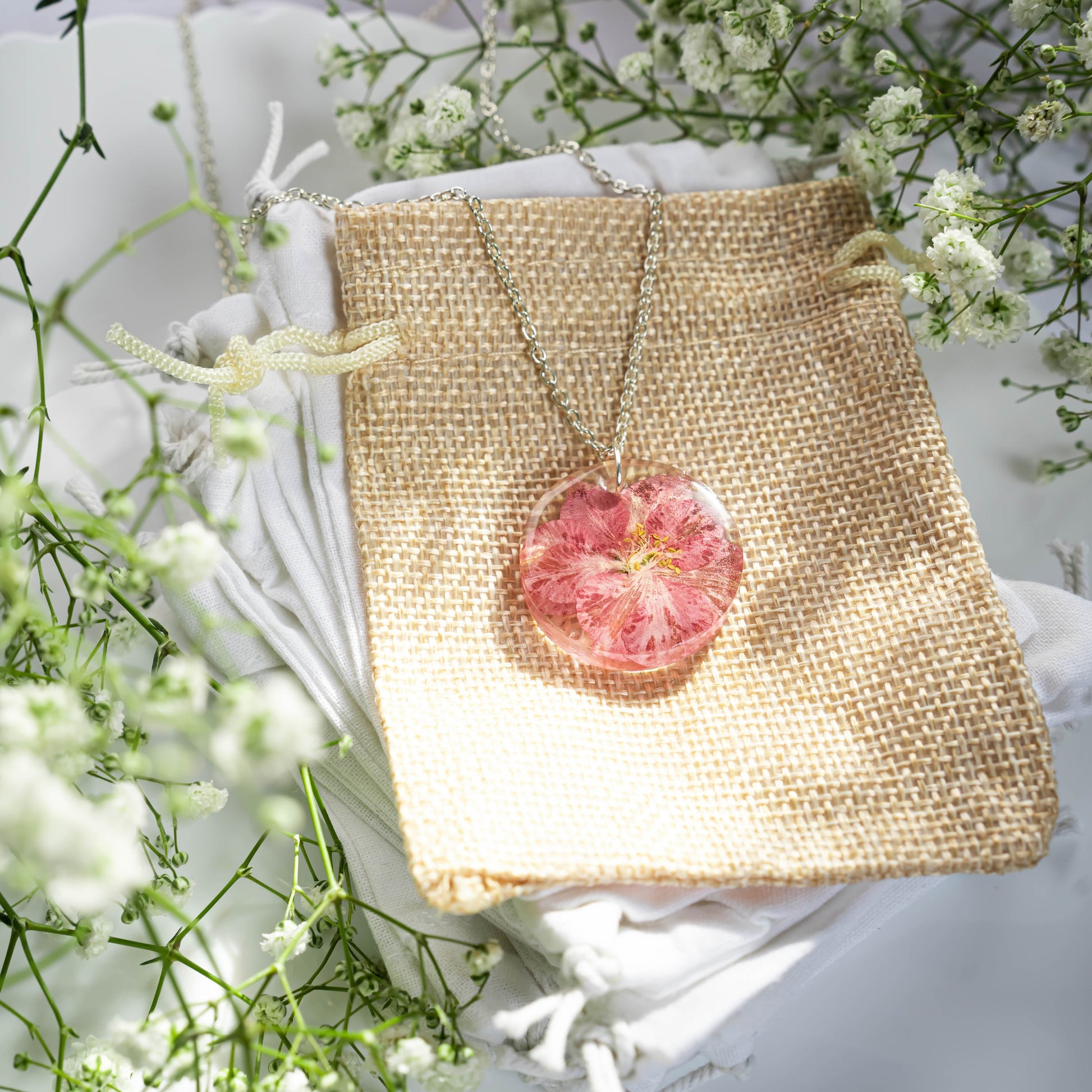 A collection of handmade resin art pendants, showcasing intricate floral designs preserved in clear resin, attached to delicate necklaces.