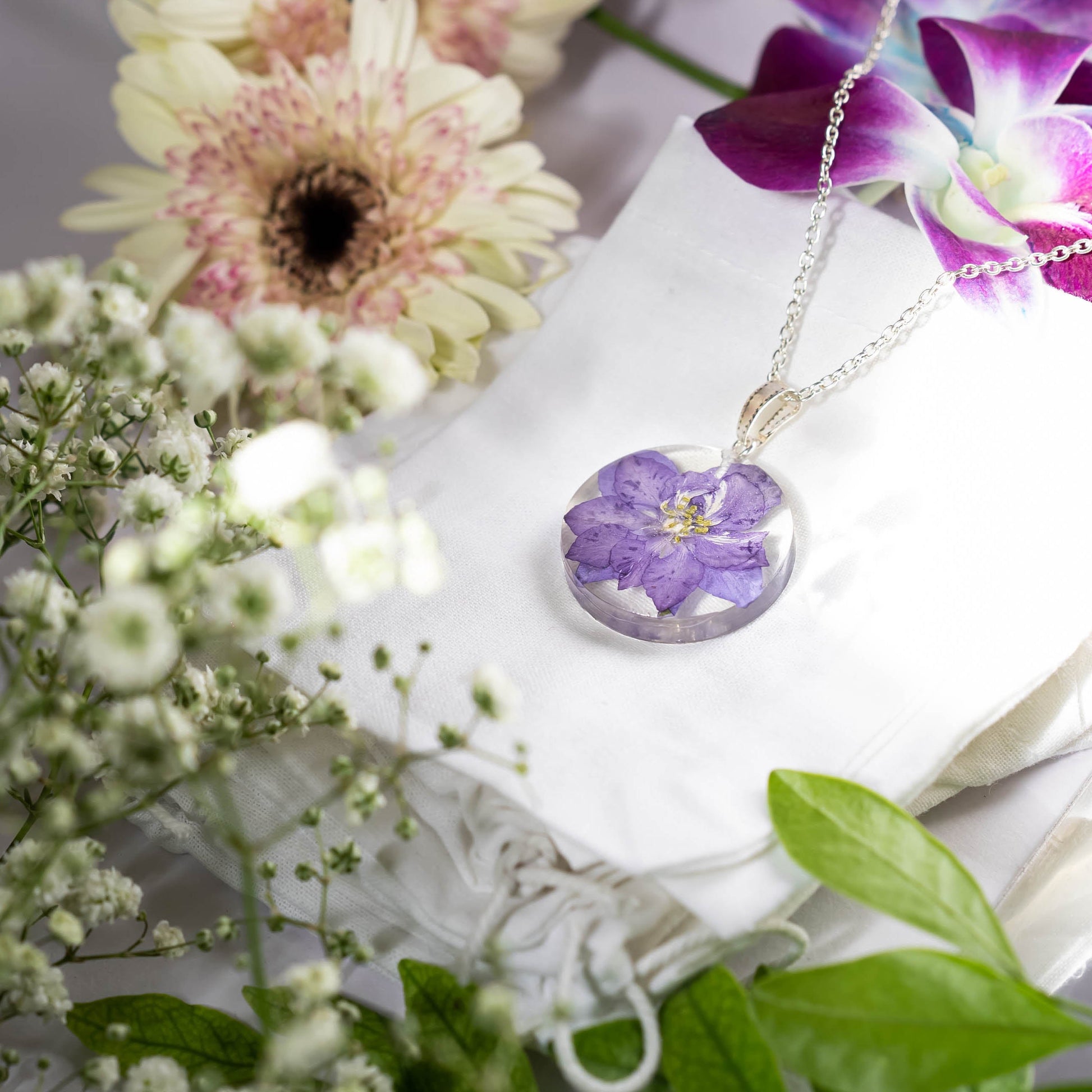 A collection of handmade resin art pendants, showcasing intricate floral designs preserved in clear resin, attached to delicate necklaces.