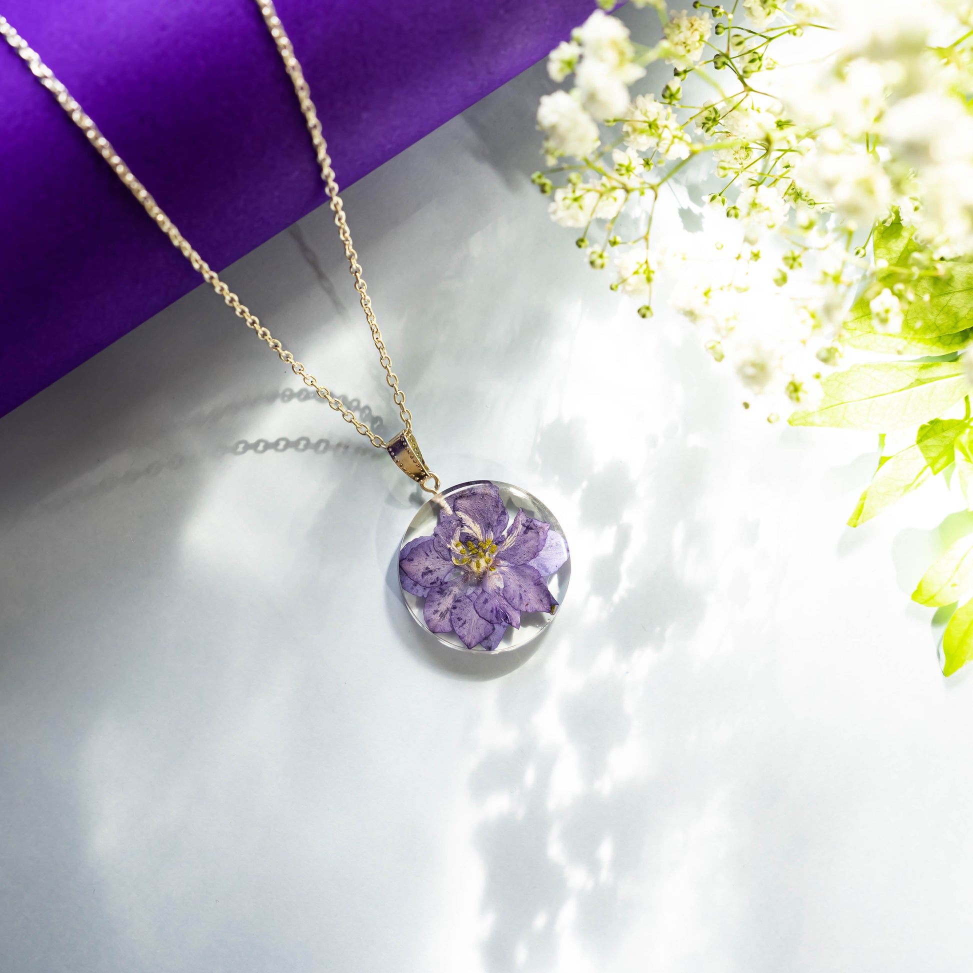 A collection of handmade resin art pendants, showcasing intricate floral designs preserved in clear resin, attached to delicate necklaces.