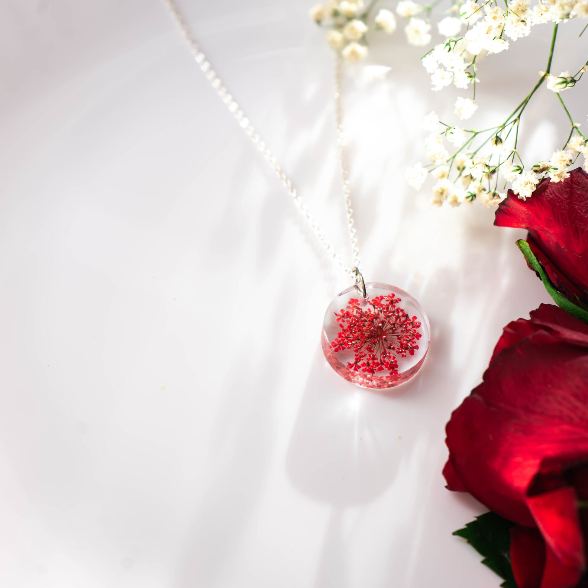 A collection of handmade resin art pendants, showcasing intricate floral designs preserved in clear resin, attached to delicate necklaces.
