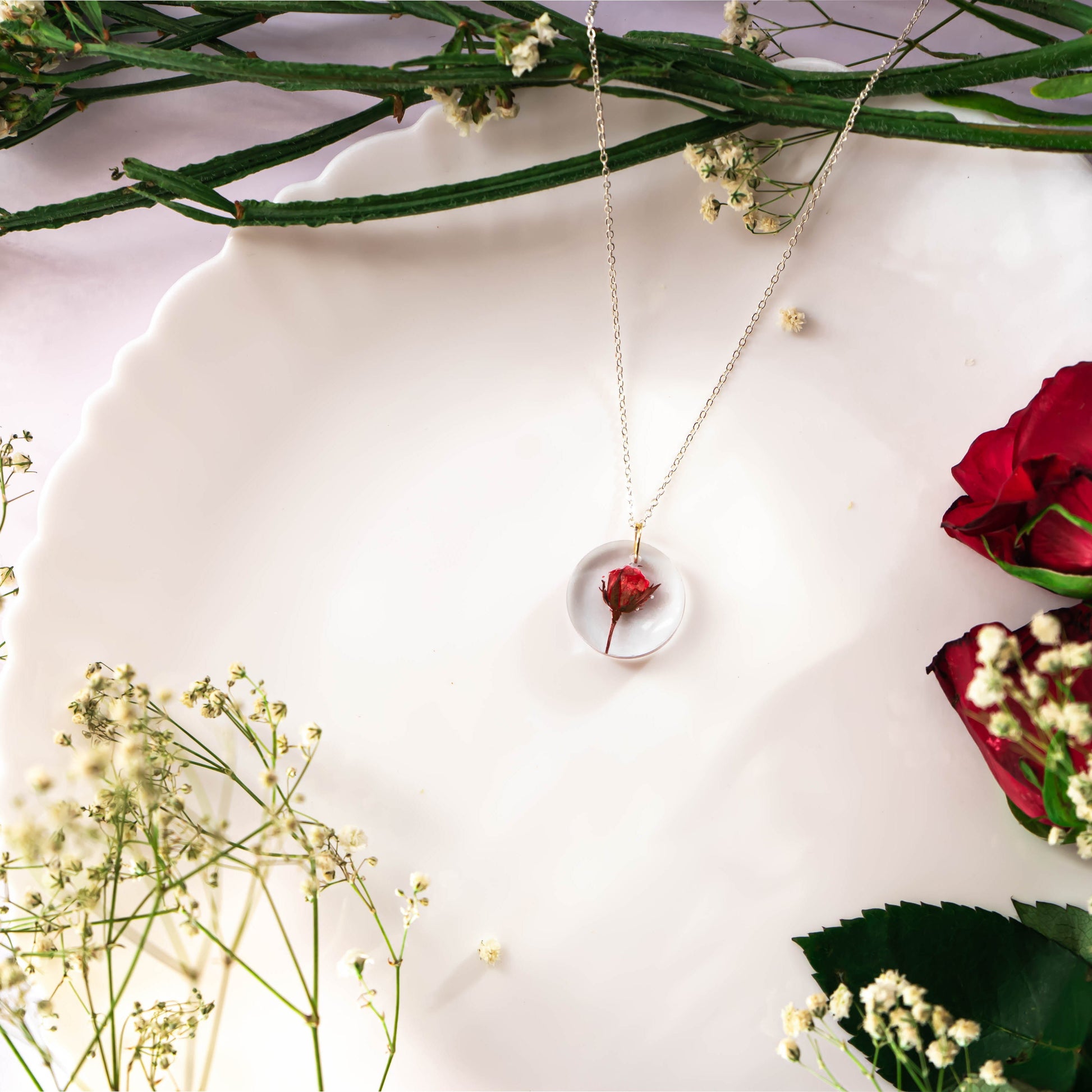 A collection of handmade resin art pendants, showcasing intricate floral designs preserved in clear resin, attached to delicate necklaces.