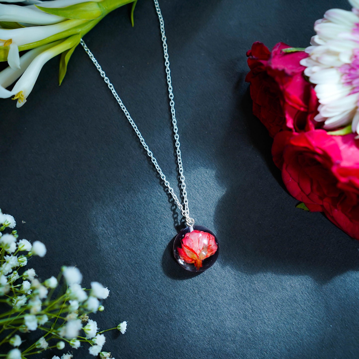 A collection of handmade resin art pendants, showcasing intricate floral designs preserved in clear resin, attached to delicate necklaces.