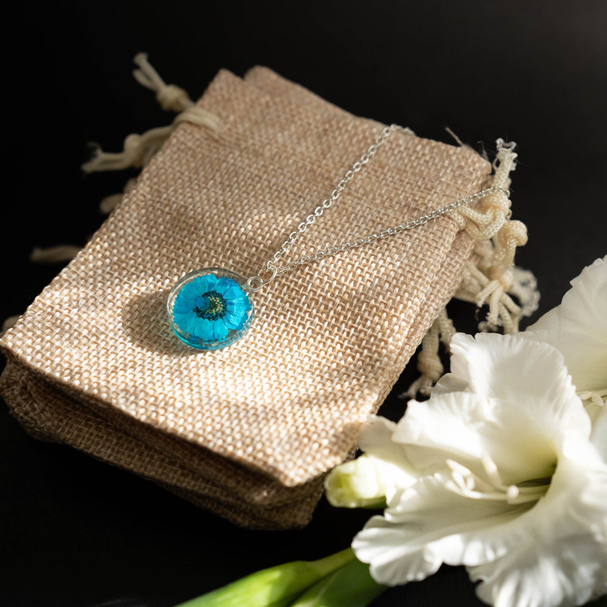 A collection of handmade resin art pendants, showcasing intricate floral designs preserved in clear resin, attached to delicate necklaces.