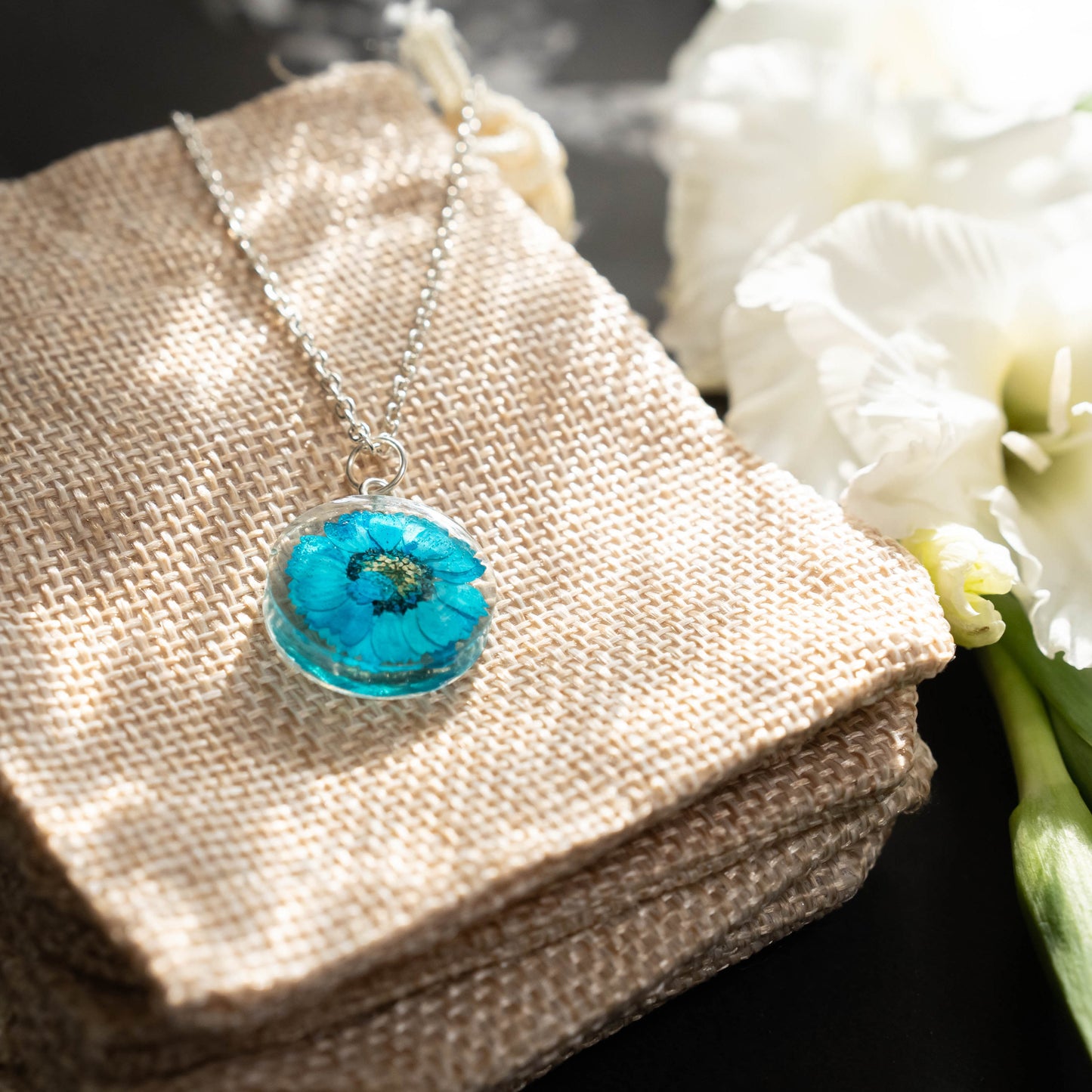 A collection of handmade resin art pendants, showcasing intricate floral designs preserved in clear resin, attached to delicate necklaces.