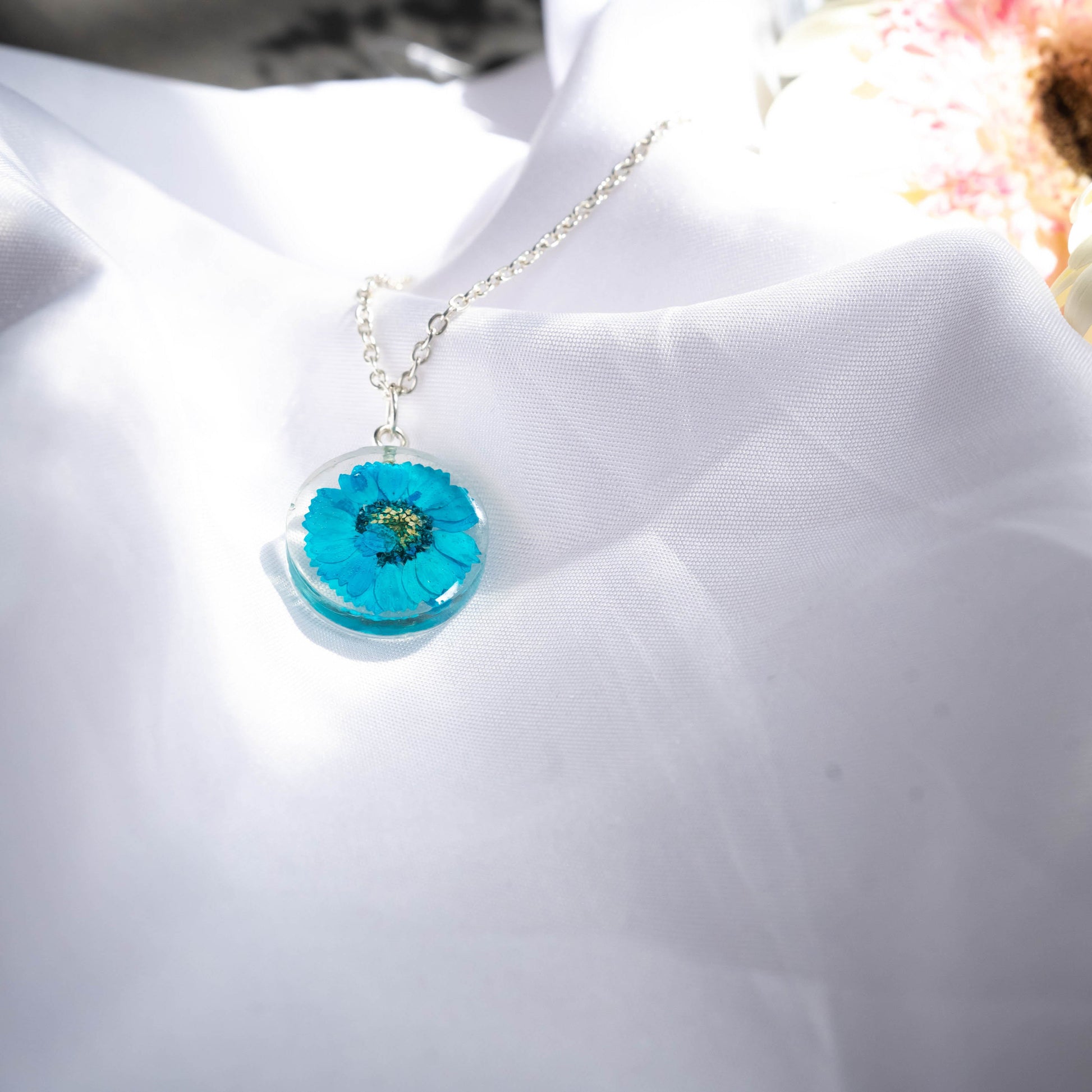 A collection of handmade resin art pendants, showcasing intricate floral designs preserved in clear resin, attached to delicate necklaces.