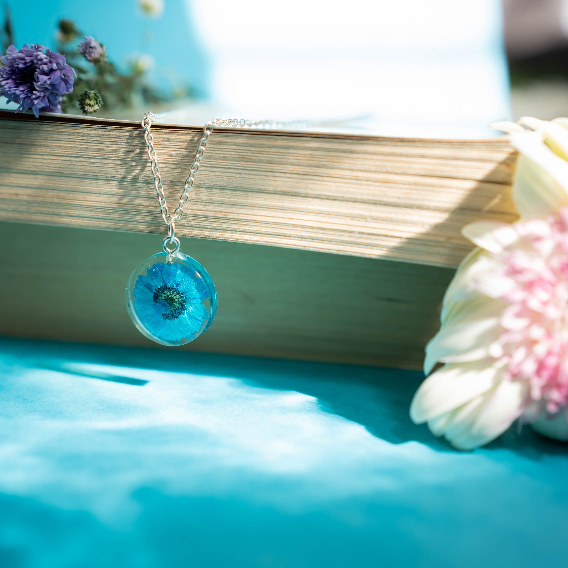 A collection of handmade resin art pendants, showcasing intricate floral designs preserved in clear resin, attached to delicate necklaces.
