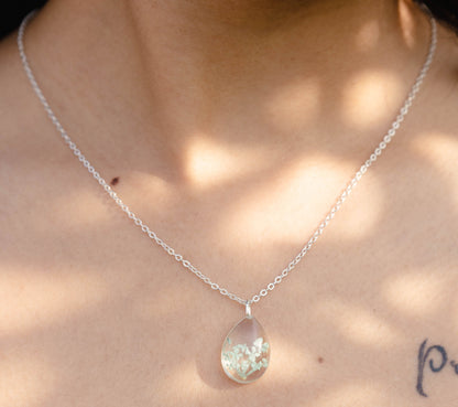 A collection of handmade resin art pendants, showcasing intricate floral designs preserved in clear resin, attached to delicate necklaces.