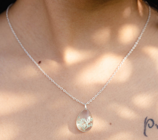 A collection of handmade resin art pendants, showcasing intricate floral designs preserved in clear resin, attached to delicate necklaces.