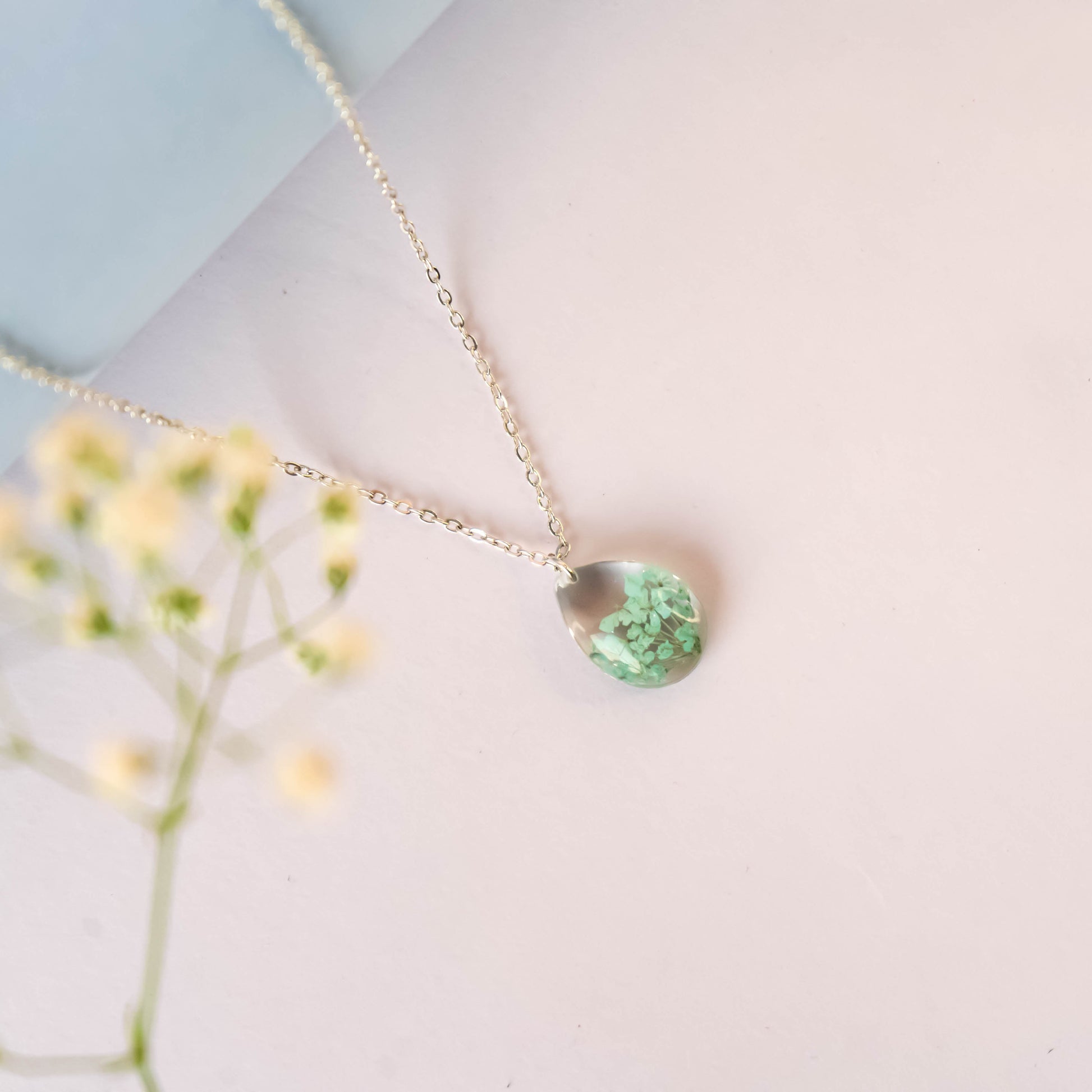 A collection of handmade resin art pendants, showcasing intricate floral designs preserved in clear resin, attached to delicate necklaces.