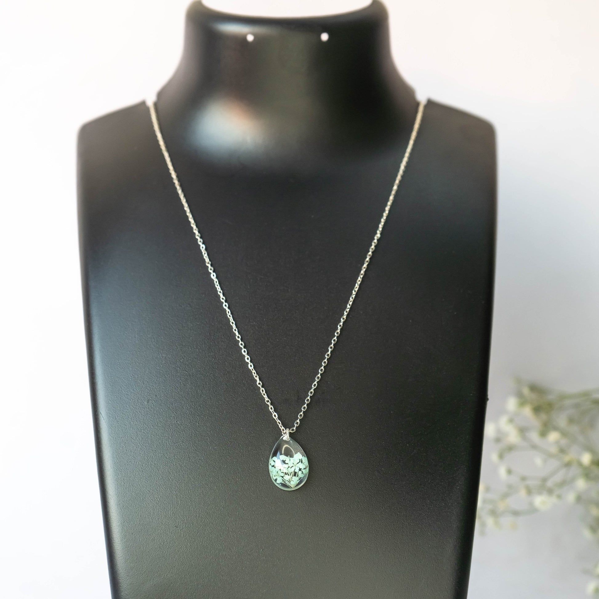 A collection of handmade resin art pendants, showcasing intricate floral designs preserved in clear resin, attached to delicate necklaces.
