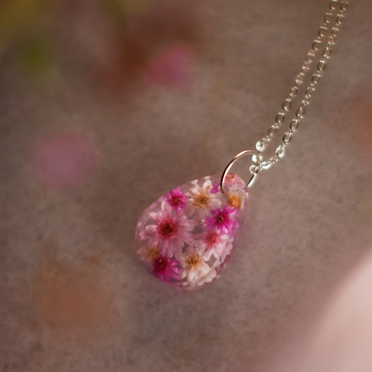A collection of handmade resin art pendants, showcasing intricate floral designs preserved in clear resin, attached to delicate necklaces.
