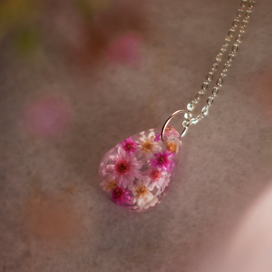 A collection of handmade resin art pendants, showcasing intricate floral designs preserved in clear resin, attached to delicate necklaces.