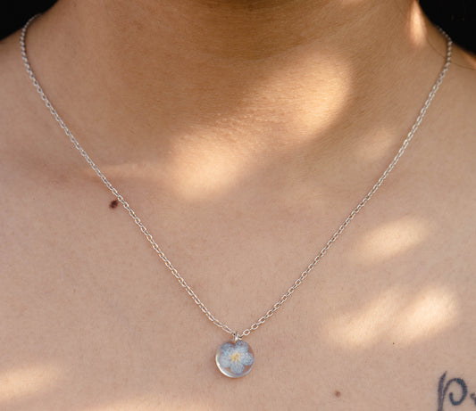 A collection of handmade resin art pendants, showcasing intricate floral designs preserved in clear resin, attached to delicate necklaces.