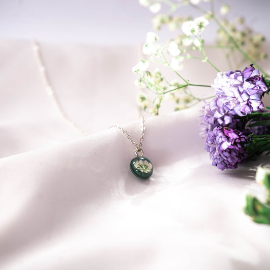 A collection of handmade resin art pendants, showcasing intricate floral designs preserved in clear resin, attached to delicate necklaces.