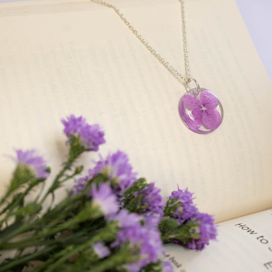 A collection of handmade resin art pendants, showcasing intricate floral designs preserved in clear resin, attached to delicate necklaces.