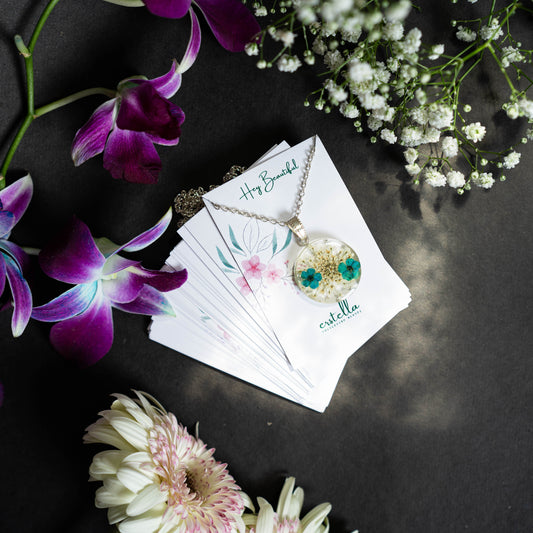 A collection of handmade resin art pendants, showcasing intricate floral designs preserved in clear resin, attached to delicate necklaces.